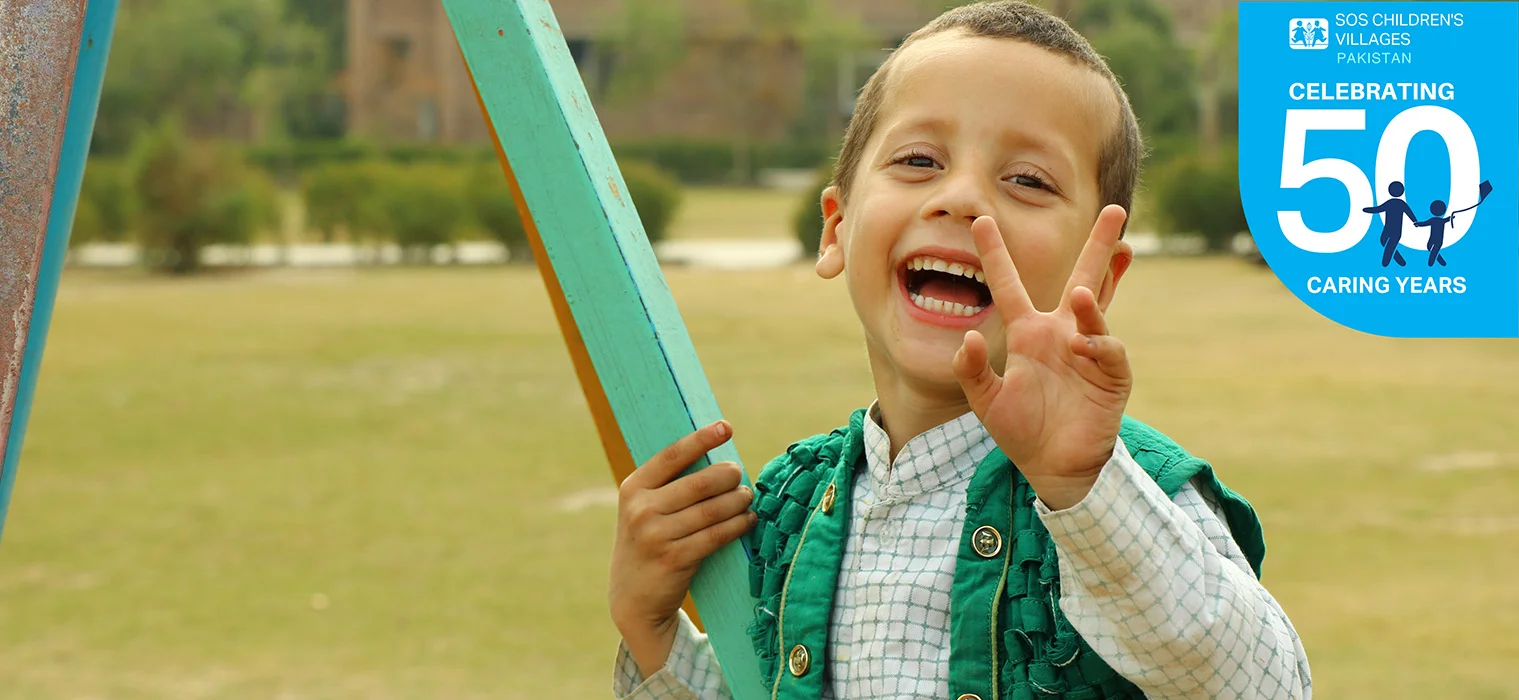 Happy girl in floral dress sits on grass, representing joy at SOS Shelter Homes in Pakistan. Colorful border with icons below.