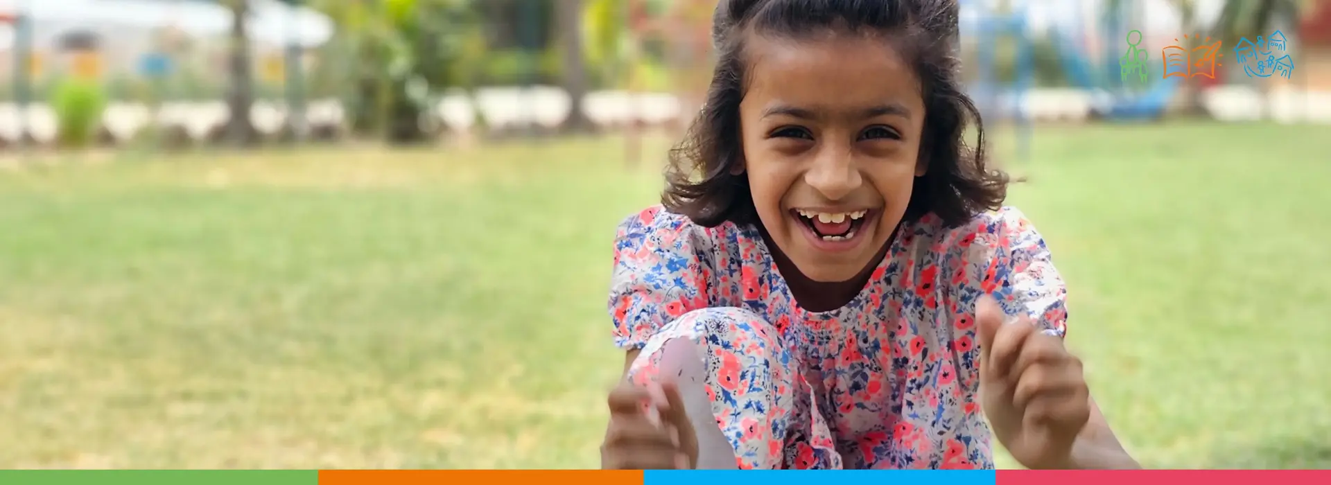 Happy girl in floral dress sits on grass, representing joy at SOS Shelter Homes in Pakistan. Colorful border with icons below.